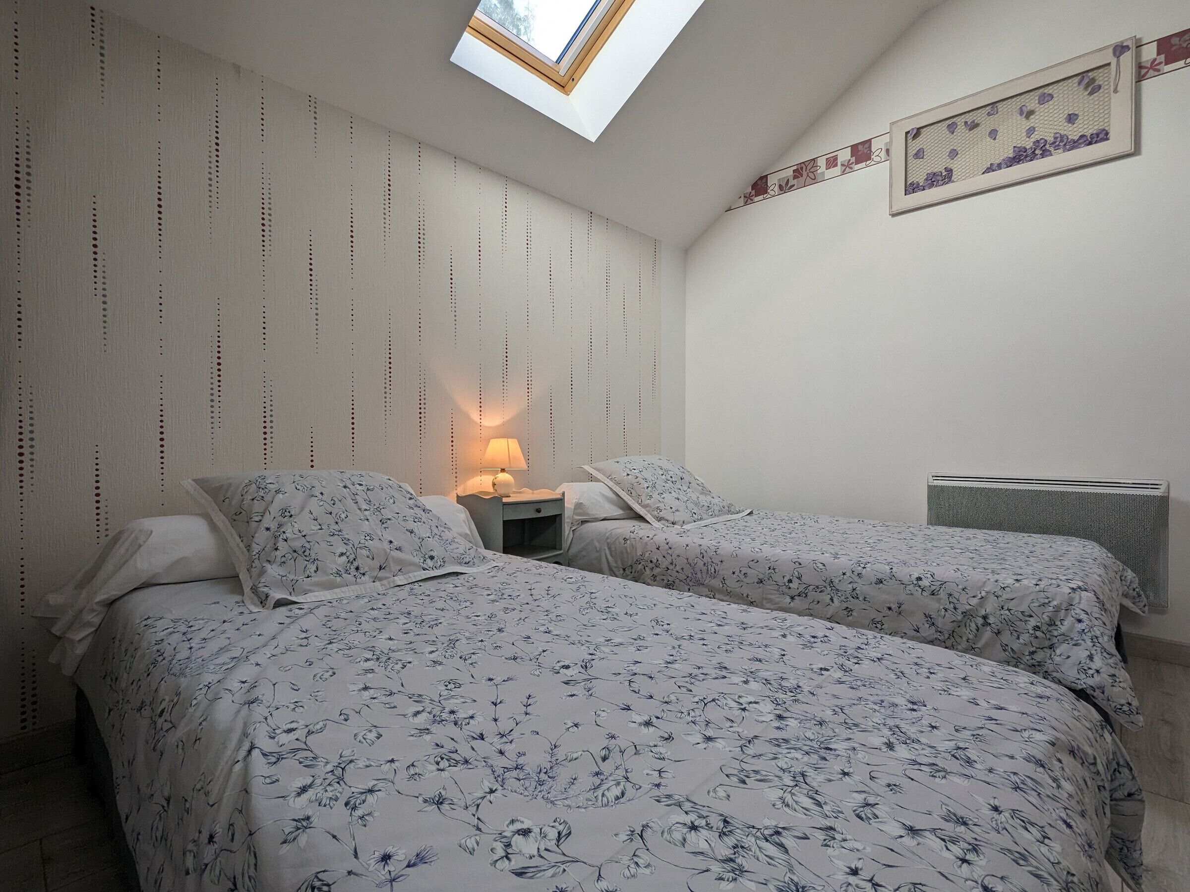 A bedroom with two beds, a skylight, a radiator, and a wall with a floral pattern.