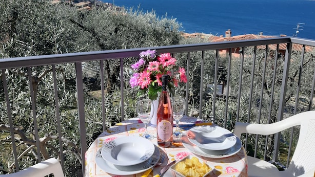 A table set with plates, a bottle of rosato wine, and a vase of flowers on a balcony overlooking the sea. - Apartment Azalea with beautiful lake view (Brenzone sul Garda)