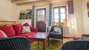 Ein gemütliches Wohnzimmer mit einem roten Sofa, einem schwarzen Sessel, einem Holztisch und einem Landschaftsbild.
