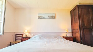 Een slaapkamer met een groot bed, twee nachtkastjes met lampen, een houten garderobe en een schilderij aan de muur.