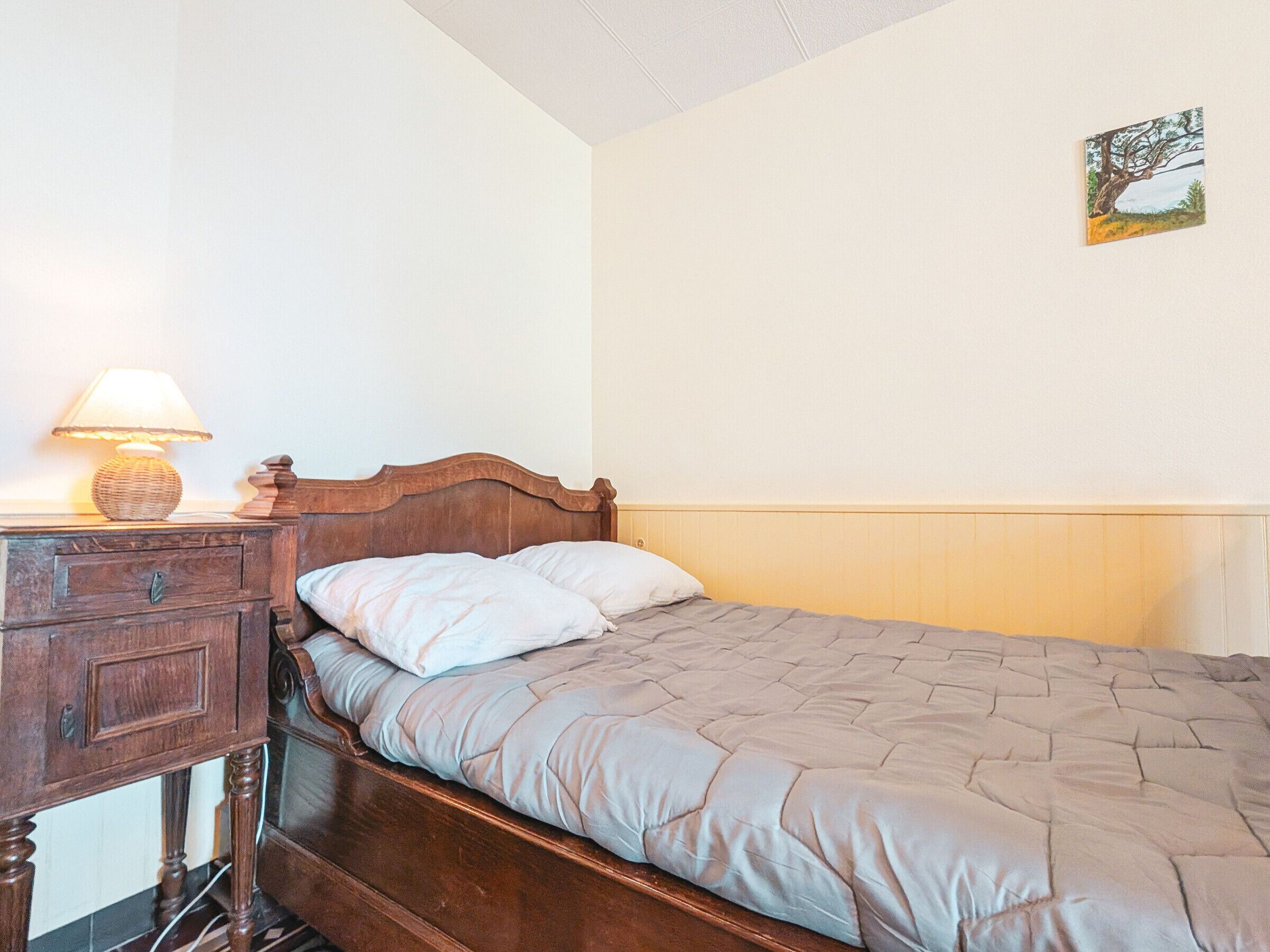 Une chambre à coucher avec un lit en bois, une table de chevet avec une lampe et un tableau accroché au mur.