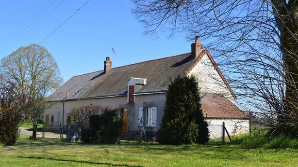 Een tweelaags huis met een schuin dak, schoorsteen en een klein terras.