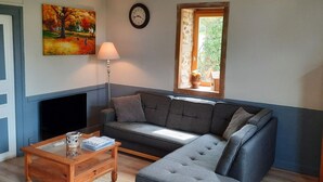 Un salon comprenant un canapé, une table basse, une lampe, un tableau, une horloge et une fenêtre donnant sur un paysage verdoyant.