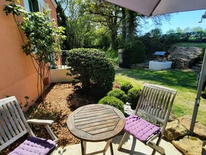 Eine Terrasse im Freien mit einem runden Holztisch und zwei weißen Stühlen mit violetten Kissen.