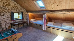 Une pièce mansardée chaleureuse, avec un lit en mezzanine, un petit bureau et une table de baby-foot.