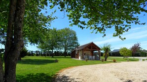 A rustic cabin with a covered patio, surrounded by a well-maintained lawn and trees. - Family & Friends Retreat: Near Loire Castles, ZooParc de Beauval, Spacious Garden, Sleeps 12 (Vicq-sur-Nahon)