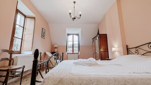 A bedroom with a large bed, a wooden chair, a radiator, a window, and a wardrobe.