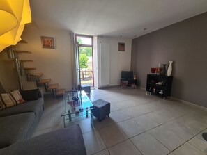 Un salon comprenant un canapé, une table basse en verre, un téléviseur, un meuble noir et une porte donnant sur l’extérieur.