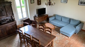 A dining area with a wooden table and chairs, a blue sofa, and a television on a wooden stand.