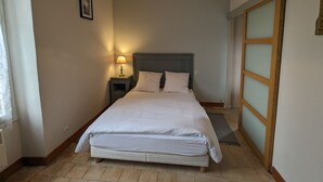 A bedroom with a bed, nightstand, lamp, and a wooden-framed window.