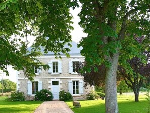 A stone building with white shutters, a central door, and a paved pathway leading to it.
