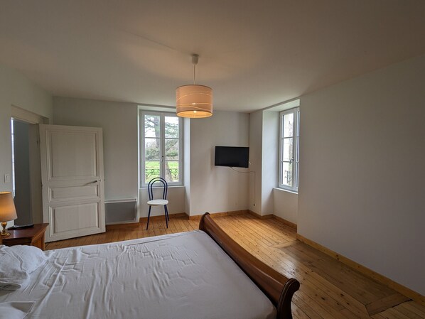 A bedroom with a bed, a chair, a TV, and a window.
