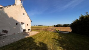 A house with a sloped roof, a chimney, and a small porch with a bench. There is a grassy yard with a swing set and a fence in the background. - Peaceful cottage in Berry, family ideal (Sainte-Fauste)