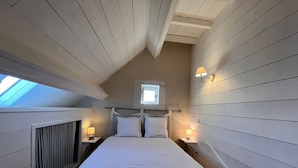 A bedroom with a sloped ceiling, a skylight, a bed with white bedding, striped pillows, and two bedside lamps. - Peaceful cottage in Berry, family ideal (Sainte-Fauste)