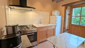 Eine Küche mit Gasherd, Backofen, Mikrowelle und Spüle. Ein Tisch und Holzschränke sind ebenfalls vorhanden.