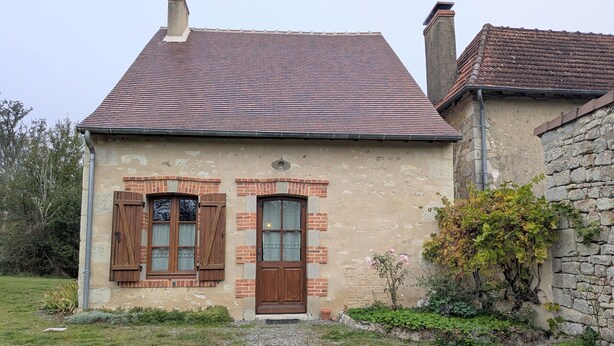 Ein rustikales Steinhaus mit Ziegeldach, zwei Holztüren und einem kleinen Garten mit Kies und Pflanzen.