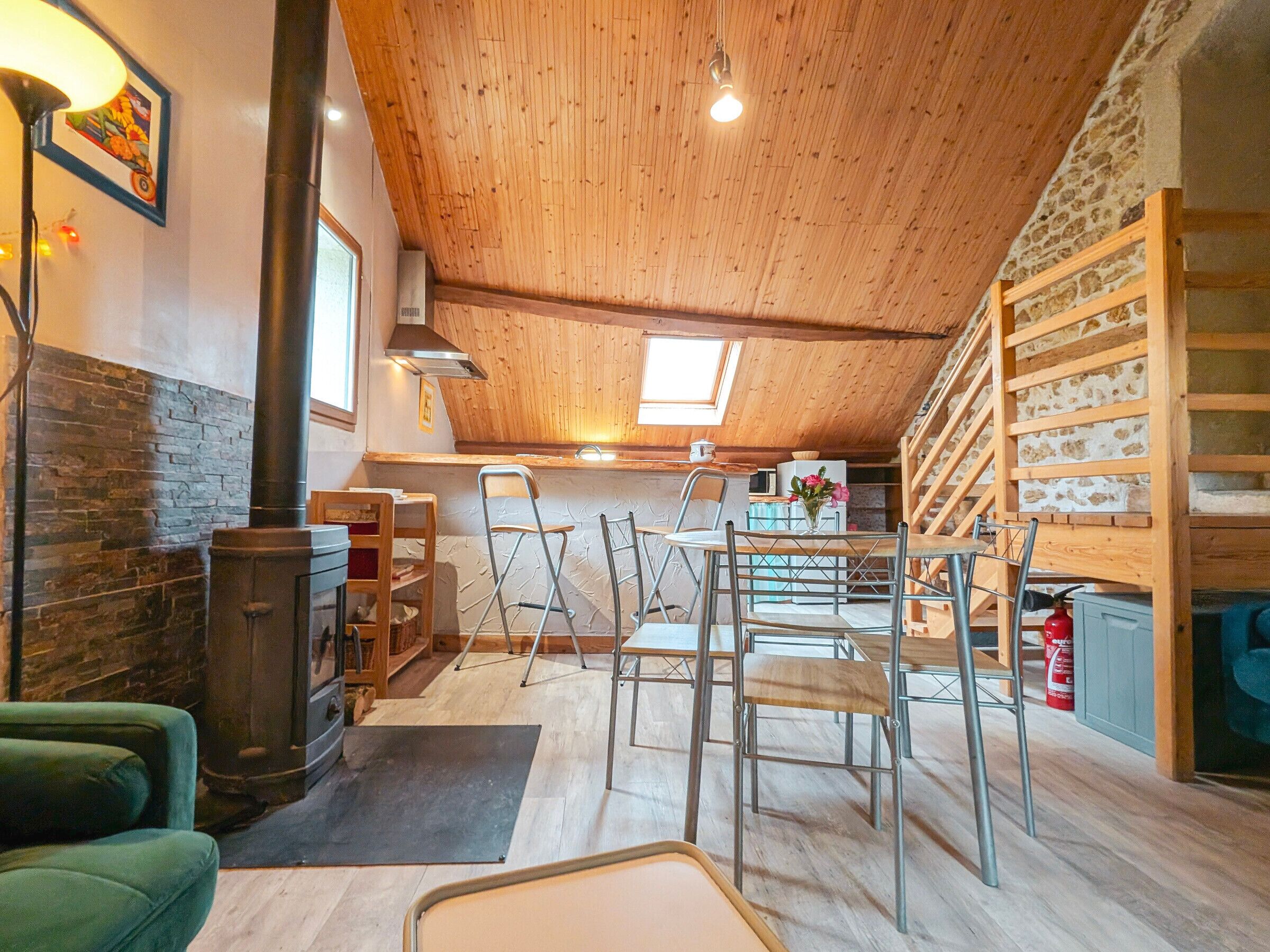 Een knus loft-achtig vertrek met houten plafond, stenen muur en een keuken met spoelbak en fornuis.