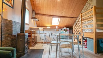 Een knus loft-achtig vertrek met houten plafond, stenen muur en een keuken met spoelbak en fornuis.