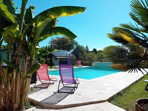 A swimming pool with lounge chairs, surrounded by tropical plants. - Charming Cottage with Heated Pool, Private Garden, Near Creuse River and Historic Villages (Le Menoux)