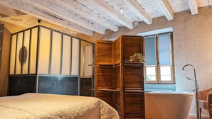 A bedroom with a bed, a wooden wardrobe, a bathtub, and a window. - Cozy Renovated Forge with Sauna, Shared Pool & Nearby Attractions (Le Menoux)