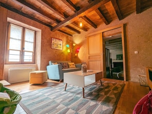 Uma sala de estar acolhedora com sofá, mesa de centro, radiador, janela com cortinas e teto com vigas aparentes.