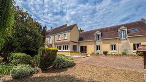 Une maison à deux étages avec une allée pavée en briques, une pelouse bien entretenue et une variété d’arbustes et d’arbres.