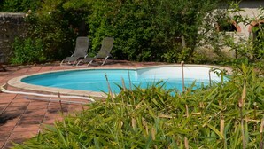 A swimming pool with two lounge chairs, surrounded by lush greenery and a stone wall. - Charming Nature Retreat with King Bed, Private Terrace, and Shared Pool in the Brenne Park (Chalais)