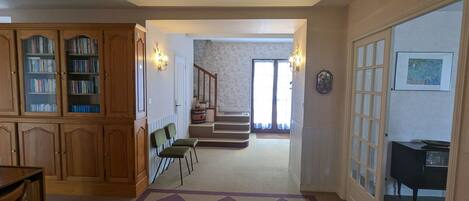 Un amplio salón con alfombra a cuadros, armarios de madera, una escalera y una mesa de comedor.