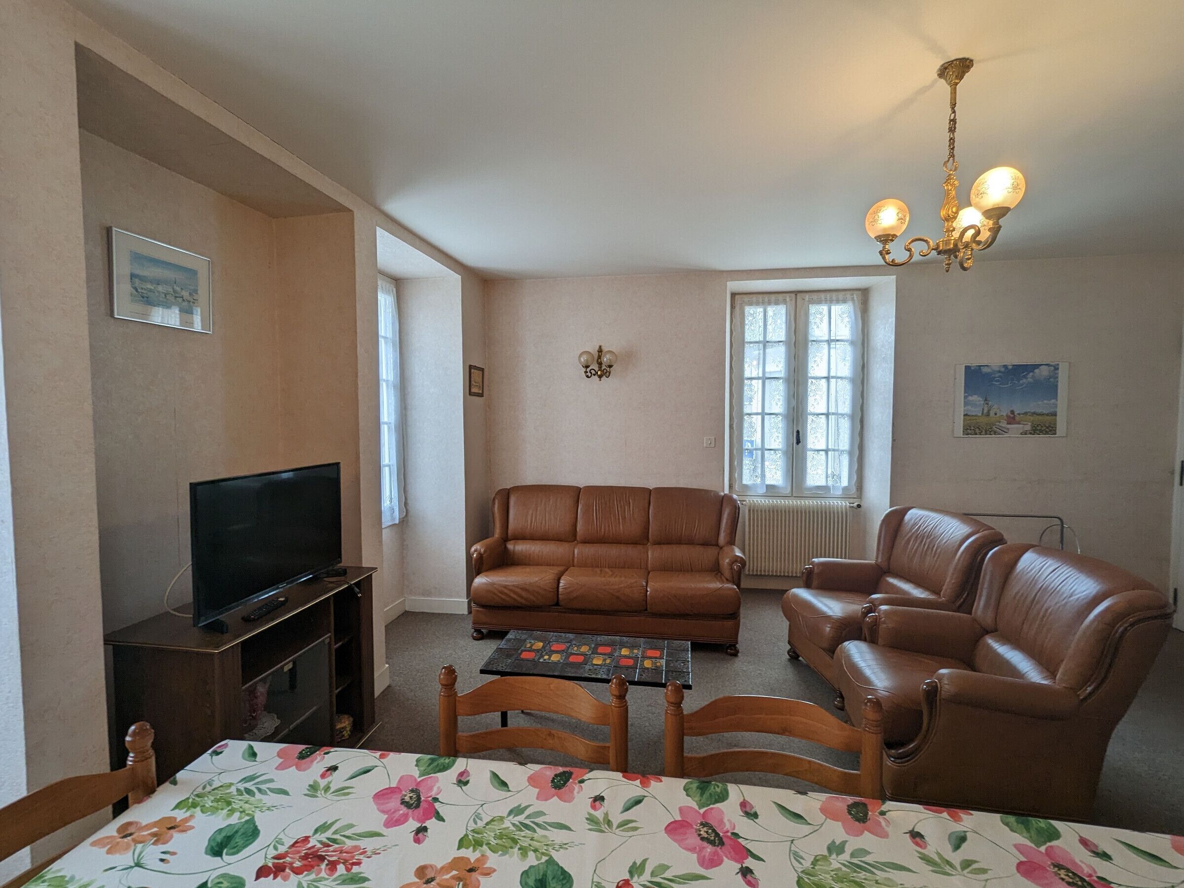 Een woonkamer met een televisie, twee banken, een tafel met stoelen en een kroonluchter.