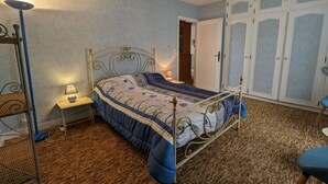 Et soveværelse med en seng med metalramme, et natbord med lampe, et garderobeskab og en stol.