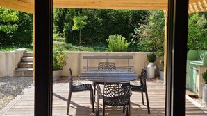 Un patio exterior con una mesa y sillas, rodeado por una terraza de madera y una pérgola.