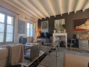 A room with a large window, a fireplace, a desk, and a chair.