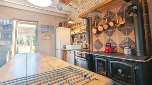 Una cocina con una mesa de madera, ollas colgantes, una estufa y un refrigerador.