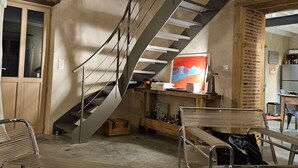 Un interior moderno con una escalera, un banco de madera, una silla metálica y una zona de cocina.