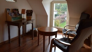 Ein gemütliches Zimmer mit schrägen Wänden, einem Holztisch mit Büchern, einem Stuhl und einem Fenster mit Blick ins Grüne.