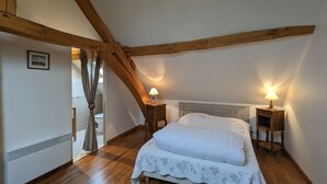 Ein Schlafzimmer mit schrägen Wänden, Holzbalken, einem Bett mit weißer Bettdecke, zwei Nachttischen mit Lampen und einem Bild an der Wand.