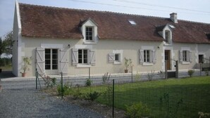 Ein zweistöckiges Haus mit Ziegeldach, weißen Außenwänden und zahlreichen Fenstern mit Fensterläden.
