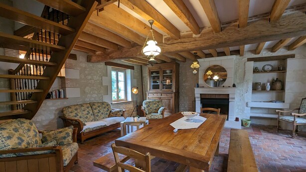 Ein rustikaler Raum mit freiliegenden Holzbalken, einem Holzesstisch mit Stühlen, einer Couch und einem Kamin.