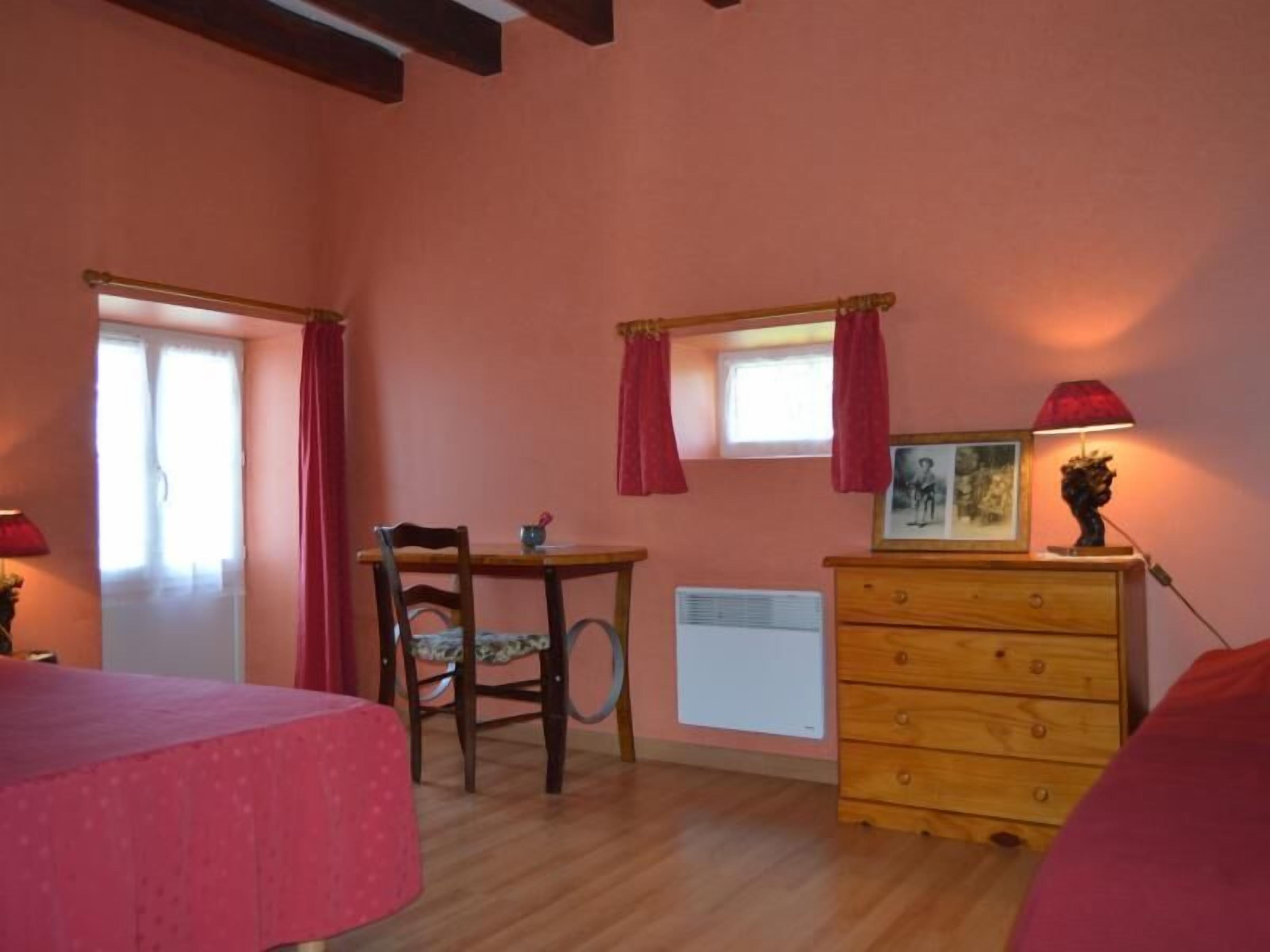 Una habitació amb una taula de fusta, una cadira, un armari i una finestra amb cortines.