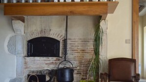 Una chimenea rústica con detalles de ladrillo, un estante de madera encima con varios recipientes, y una silla de madera a la derecha.