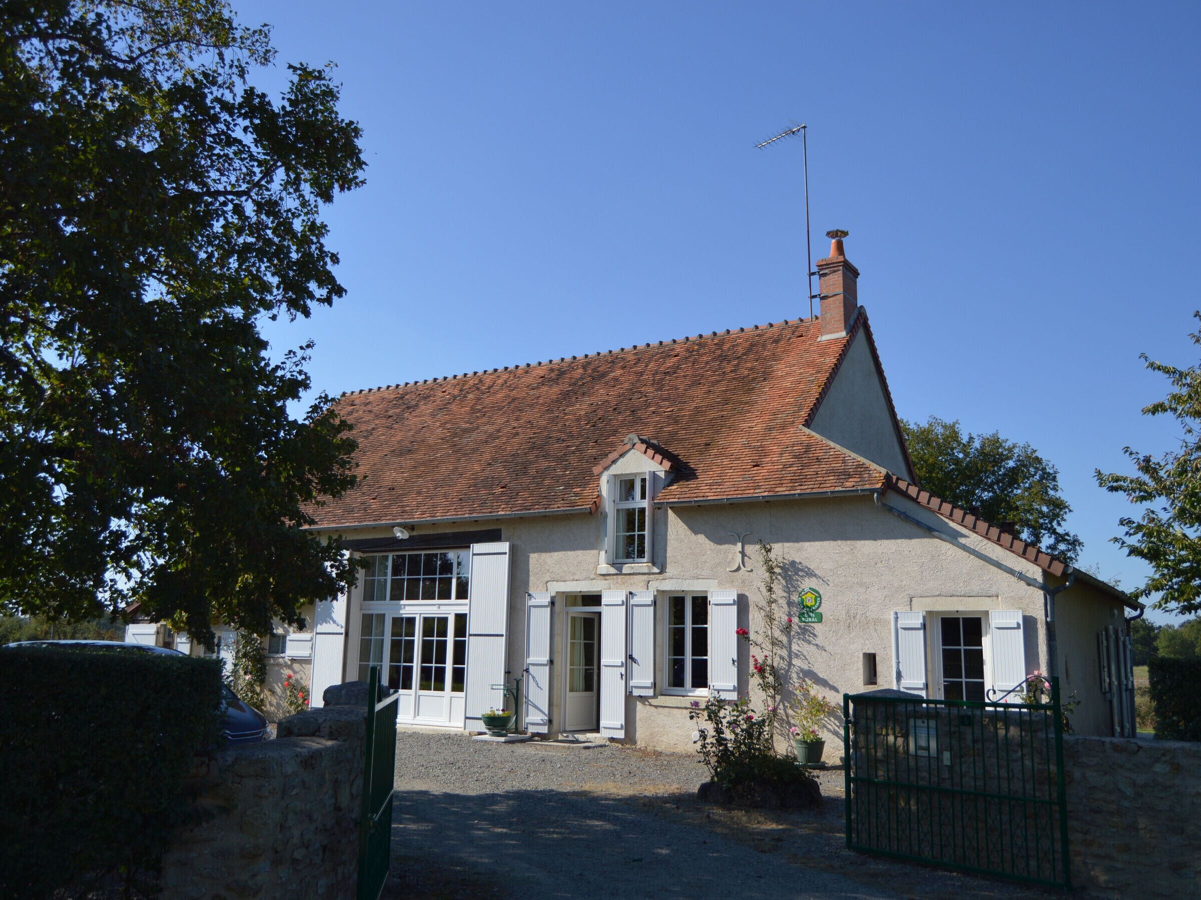 Une maison à deux étages, avec un toit en tuiles, une cheminée et un petit jardin agrémenté de plantes en pot.