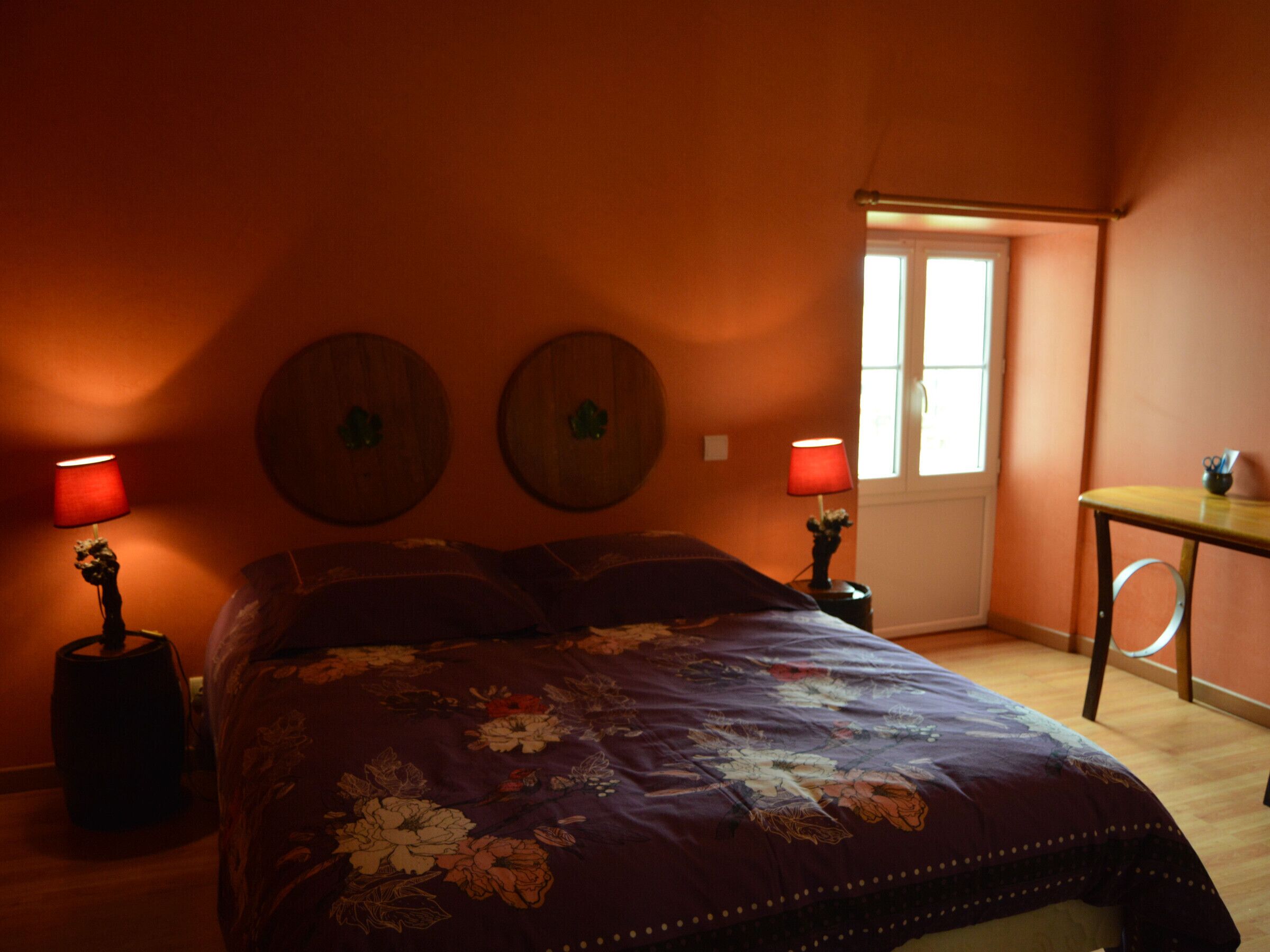 Une chambre à coucher avec un grand lit, deux horloges fixées au mur, une fenêtre et une petite table avec une lampe.