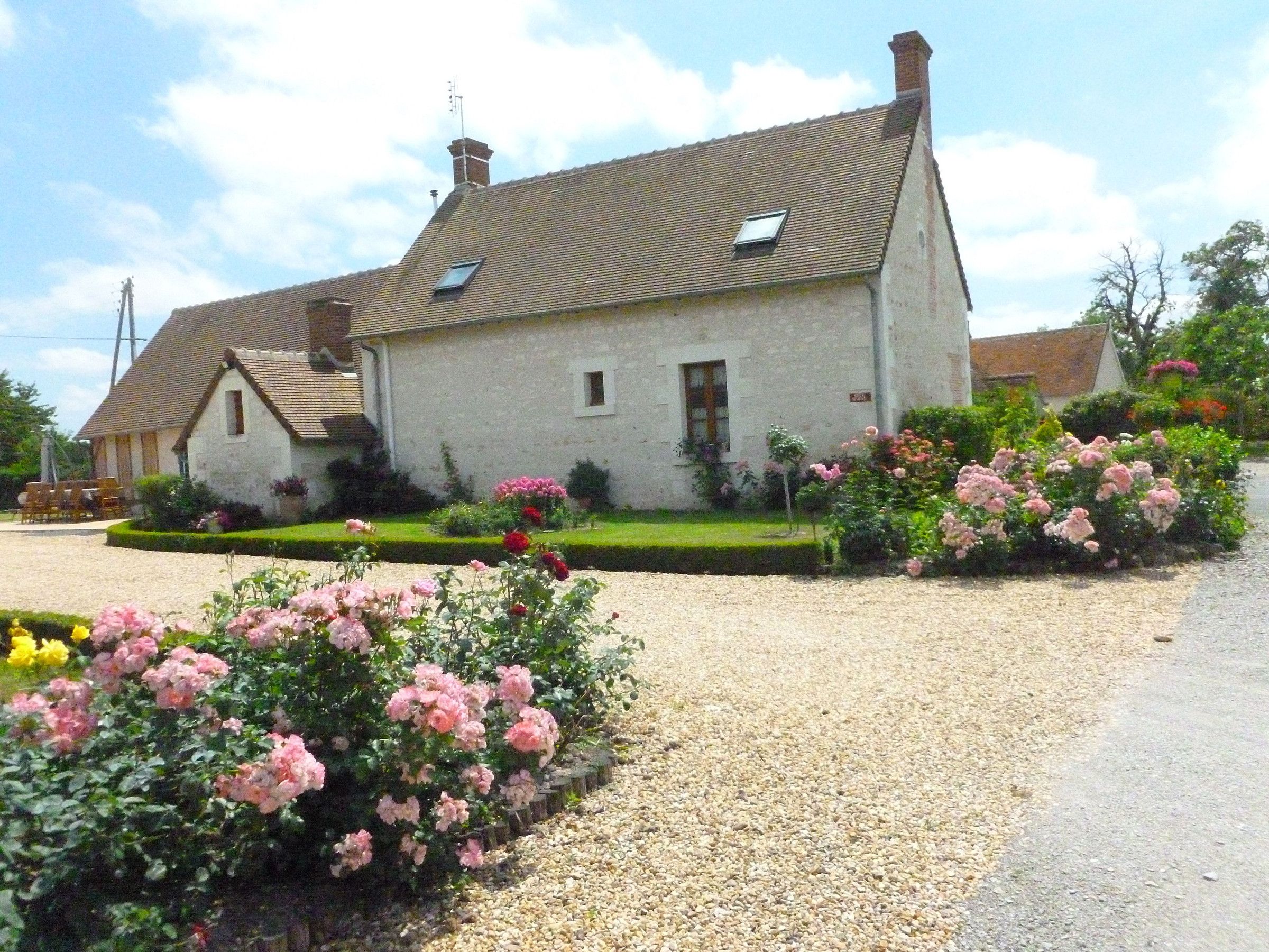 A two-story house with a gravel driveway and a garden with pink roses.