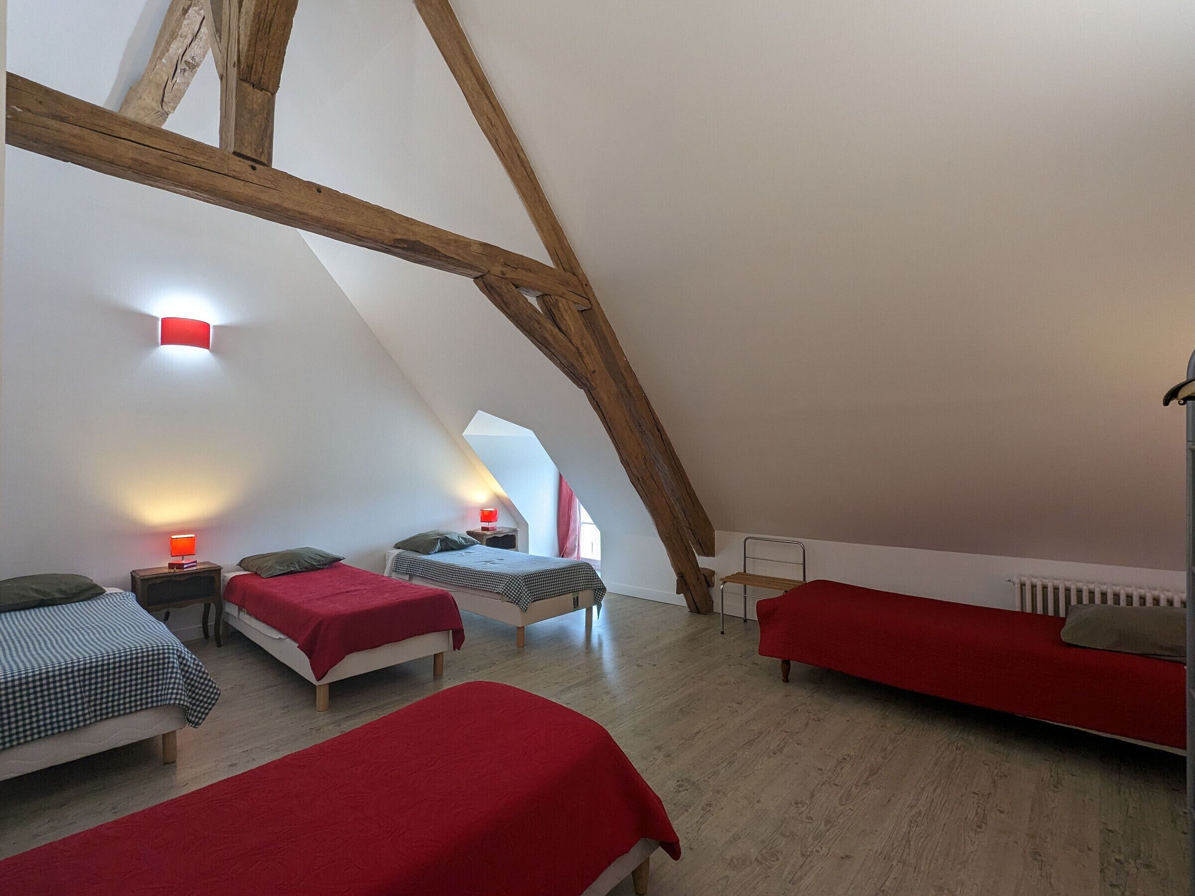 A cozy attic bedroom with two beds, a red sofa, and a red lamp.