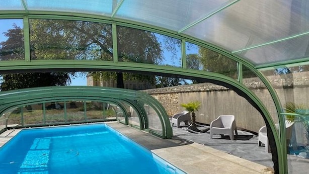 A swimming pool with a glass enclosure, surrounded by outdoor seating and a stone wall. - Charming Retreat in Berry: Heated Pool, Canoeing, Fishing, Near George Sand's House (Ardentes)