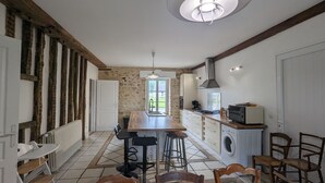 A kitchen with a central island, a dining area with a table and chairs, a washing machine, and a built-in oven. - Charming Retreat in Berry: Heated Pool, Canoeing, Fishing, Near George Sand's House (Ardentes)