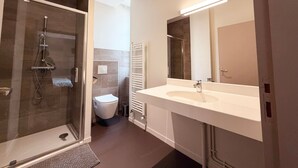 A modern bathroom with a glass-enclosed shower, a white sink, and a large mirror.