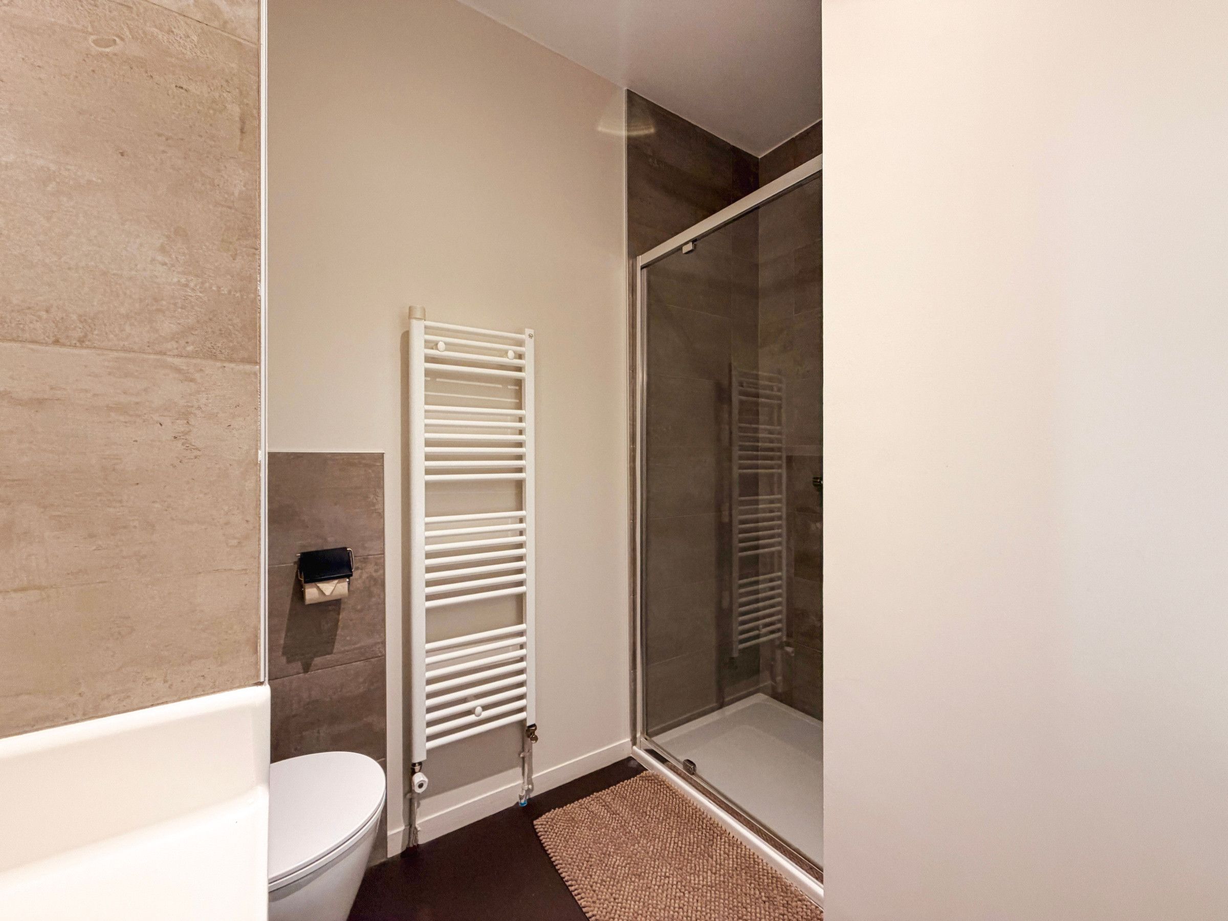 Une salle de bain comprenant des toilettes, une douche avec une porte en verre et un porte-serviettes.