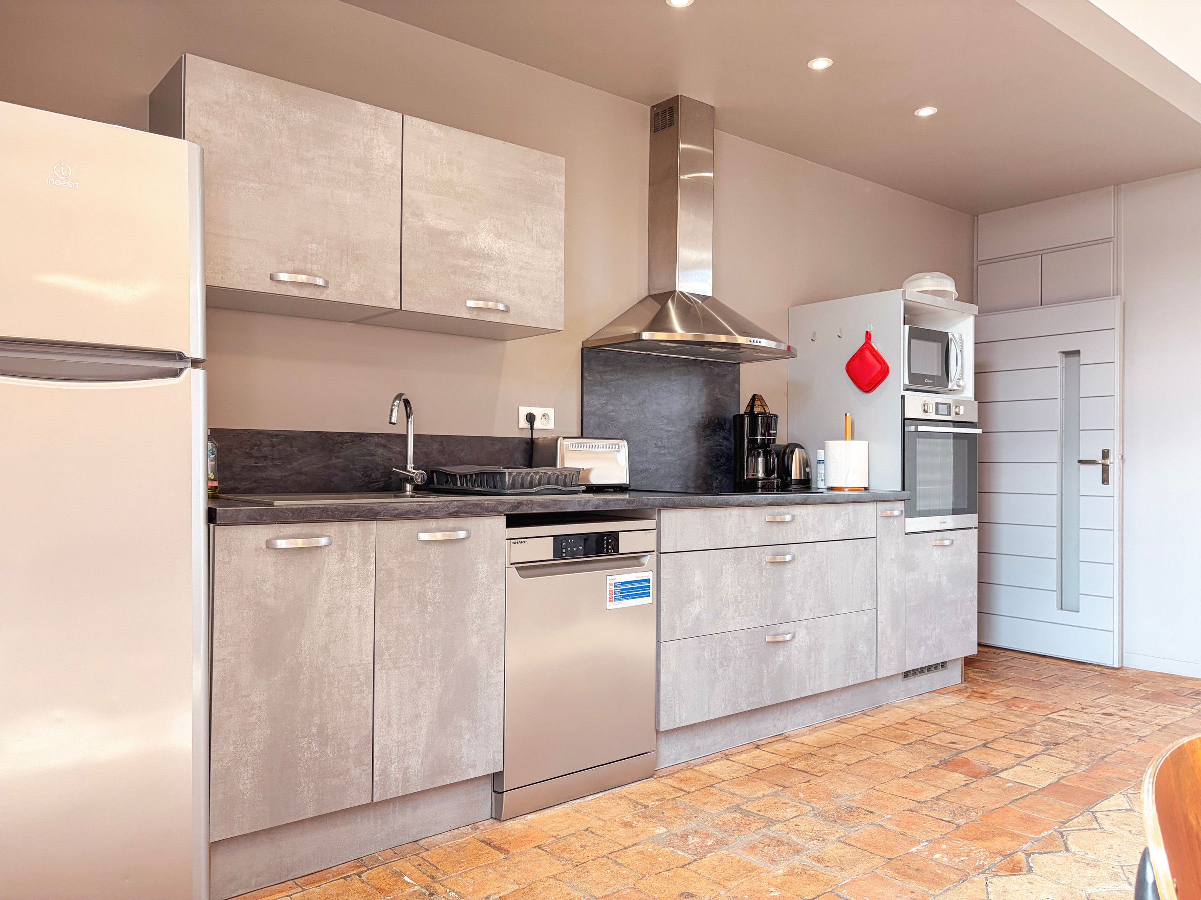 Een moderne keuken met roestvrijstalen apparatuur, grijze kastjes en een betegelde vloer.