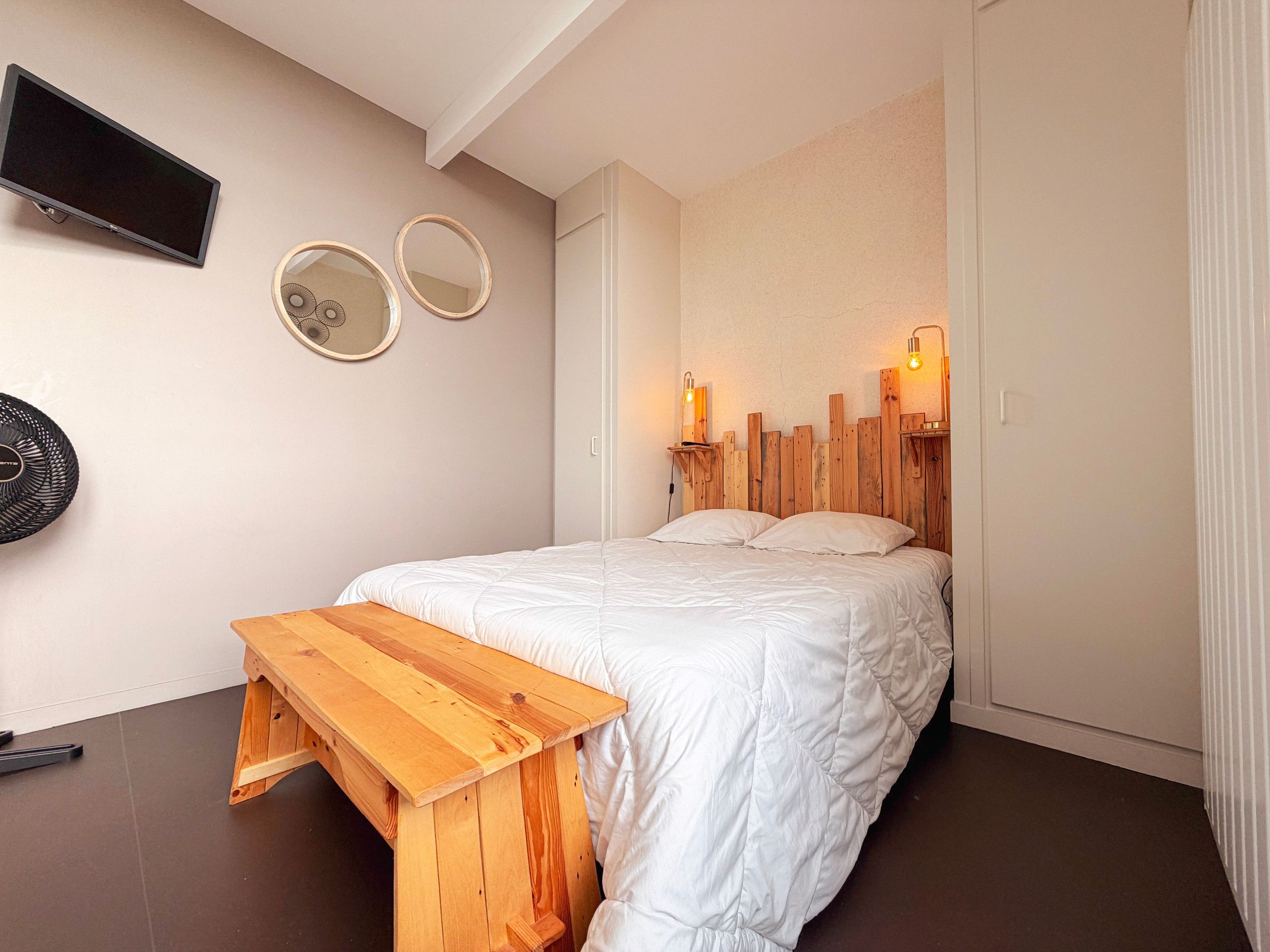 Een slaapkamer met een bed, een houten bankje, een flatscreen-tv, twee spiegels aan de muur en een hoofdbord met ingebouwde verlichting.